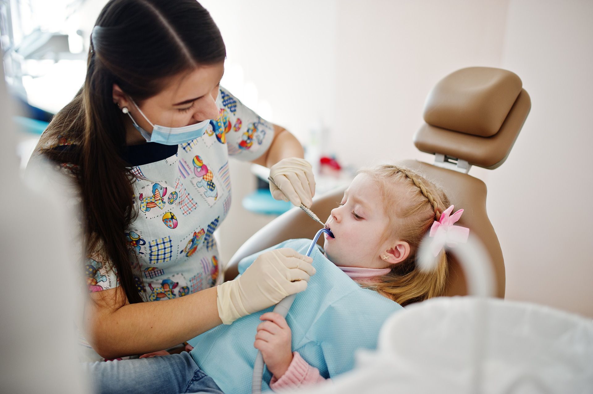 Dentist examining a child's teeth in a dental chair; the dentist wears a mask and gloves. Dentist examining a child's teeth in a dental chair; the dentist wears a mask and gloves.