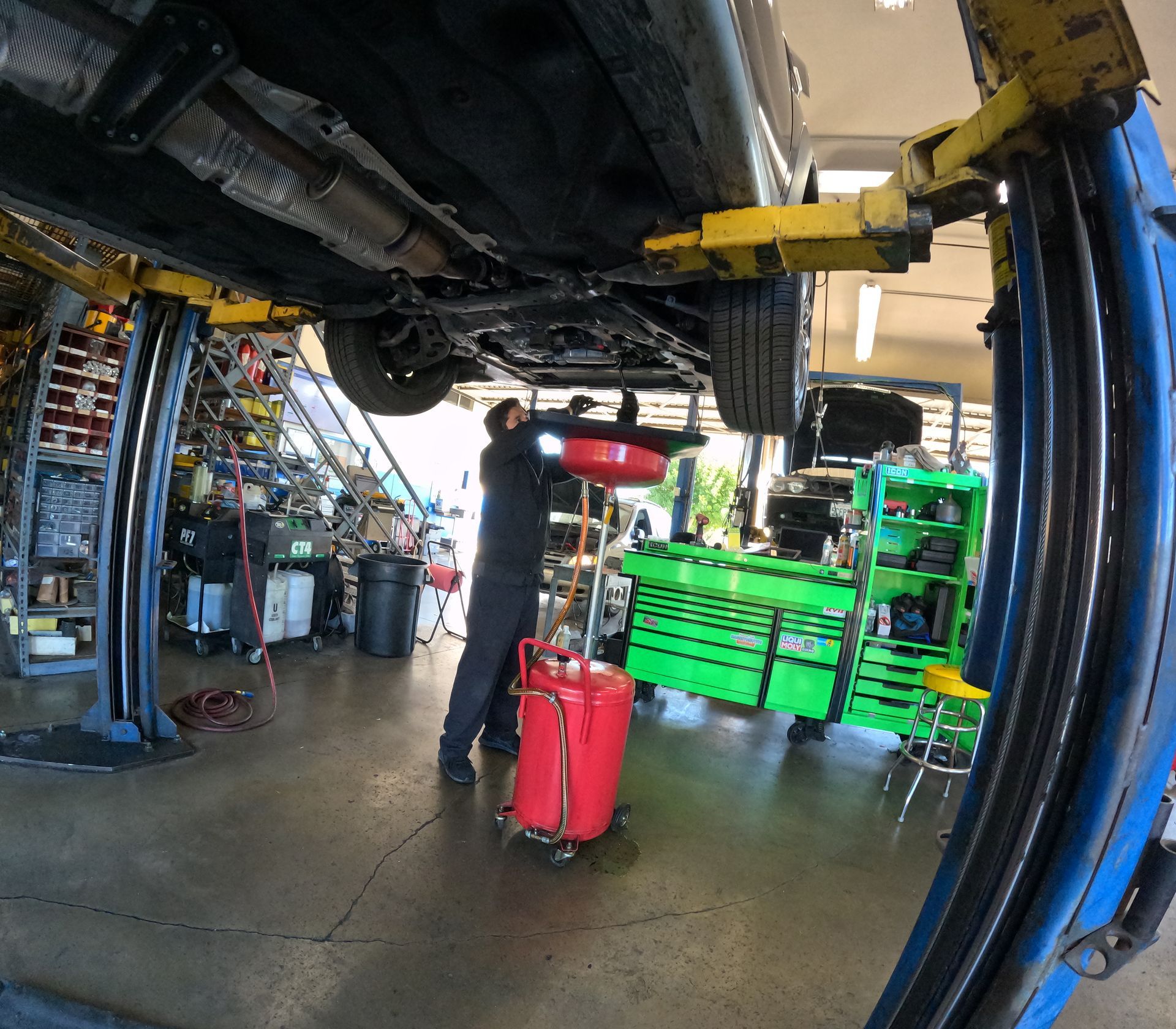 Mechanic draining oil from a car on a lift in a repair shop. | Super Service of Pomona Valley