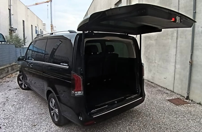 Un furgone Mercedes-Benz Classe V nero parcheggiato all'aperto su un piazzale ghiaioso con il portellone posteriore completamente aperto.