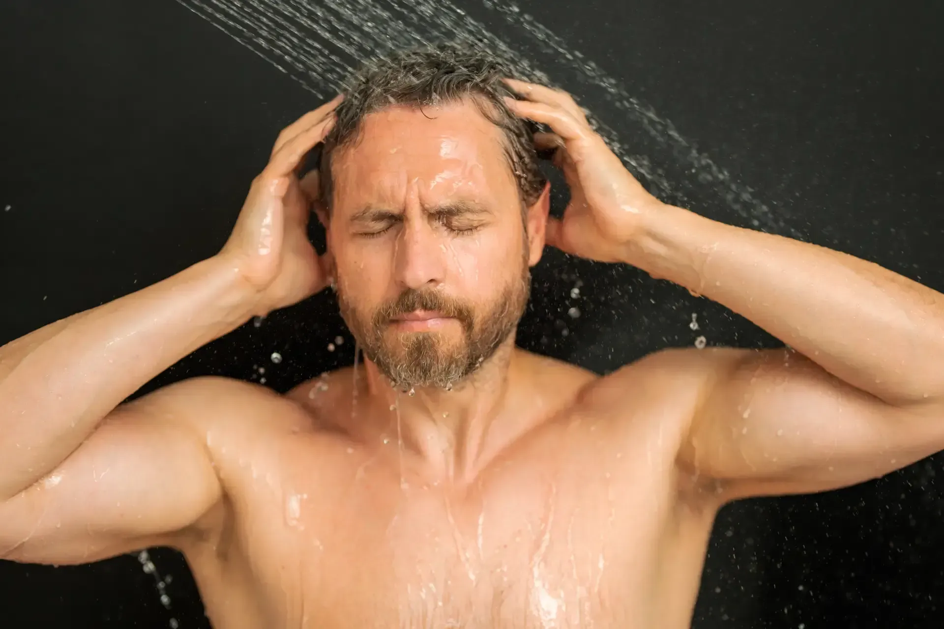A person sprays a golden hair oil mist onto their dark, curly hair.