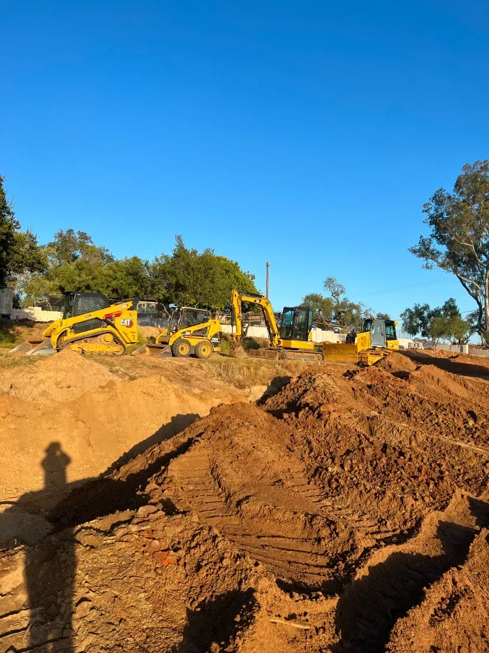 Construction site with yellow excavators on a pile of dirt under a blue sky.