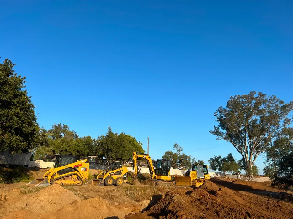 Construction site with yellow machinery, a blue sky, and dirt mounds.