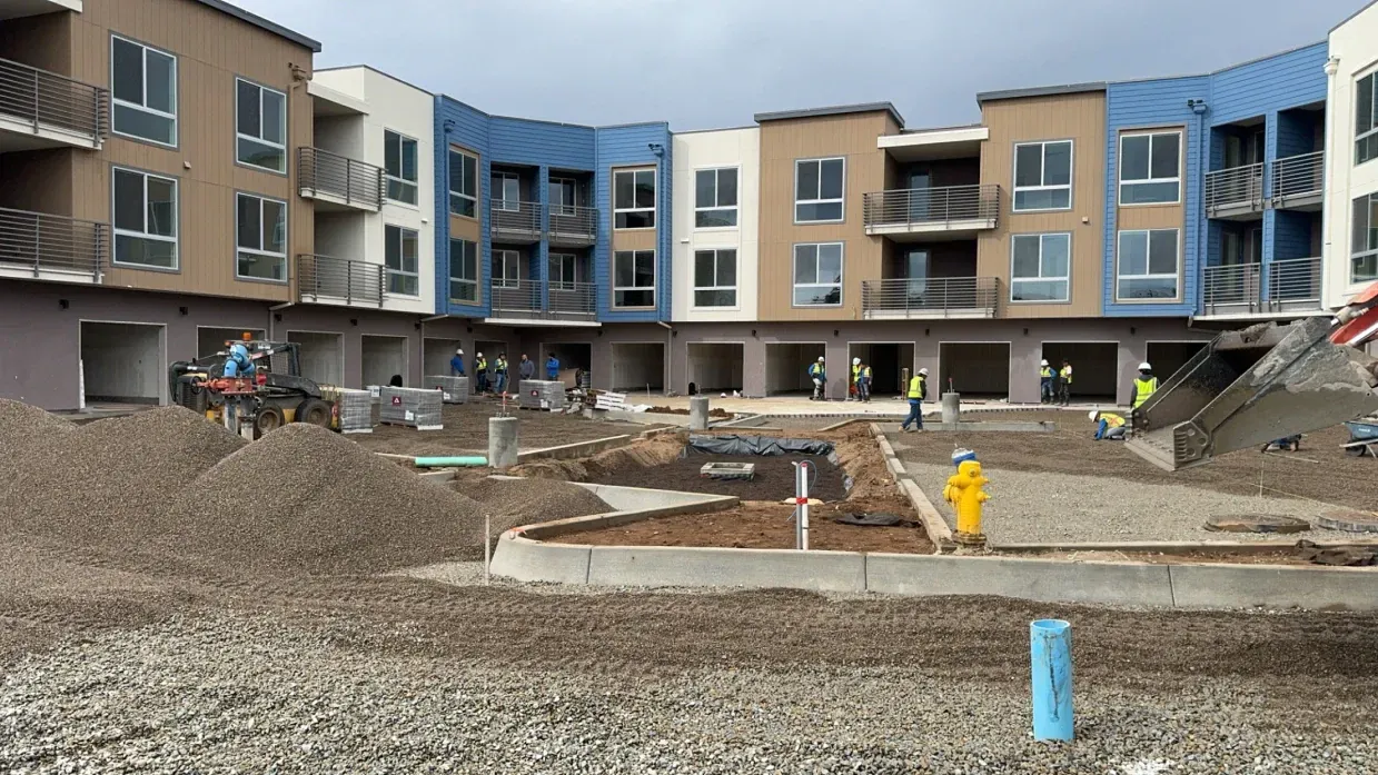 Construction site with building, gravel, and workers in blue and yellow vests.
