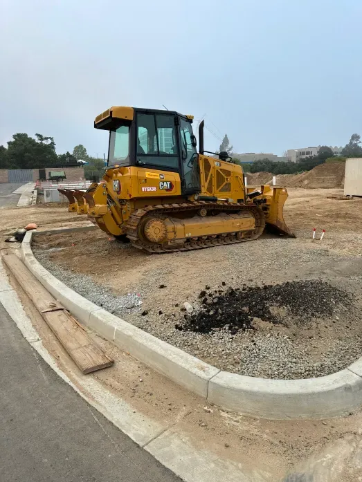 Yellow bulldozer on a dirt lot near a curb. Construction site on a hazy day.