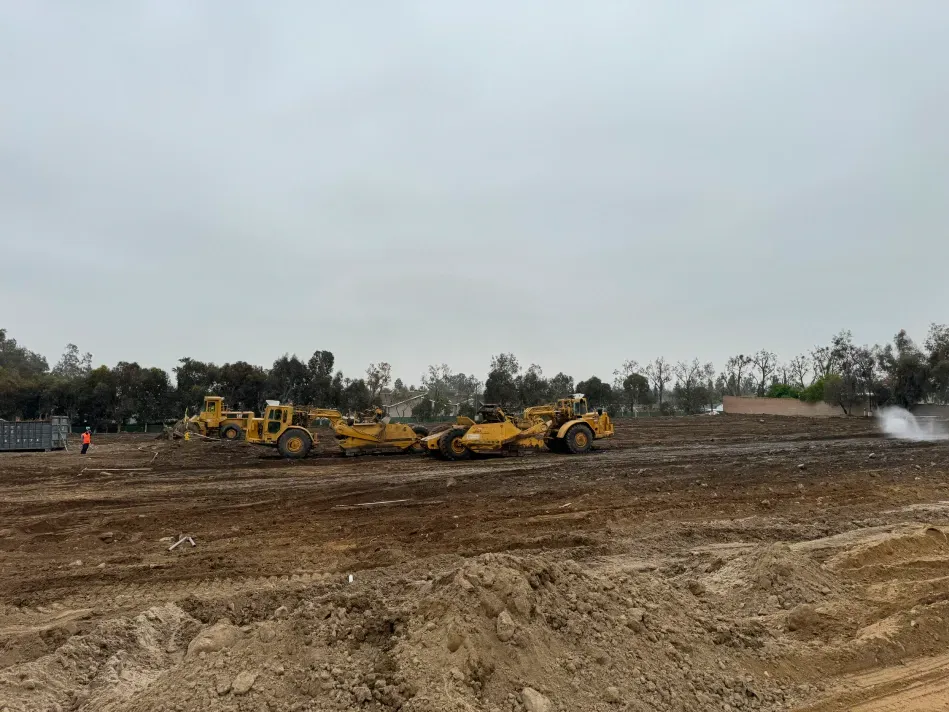 Construction site with yellow earthmovers clearing dirt under a cloudy sky.