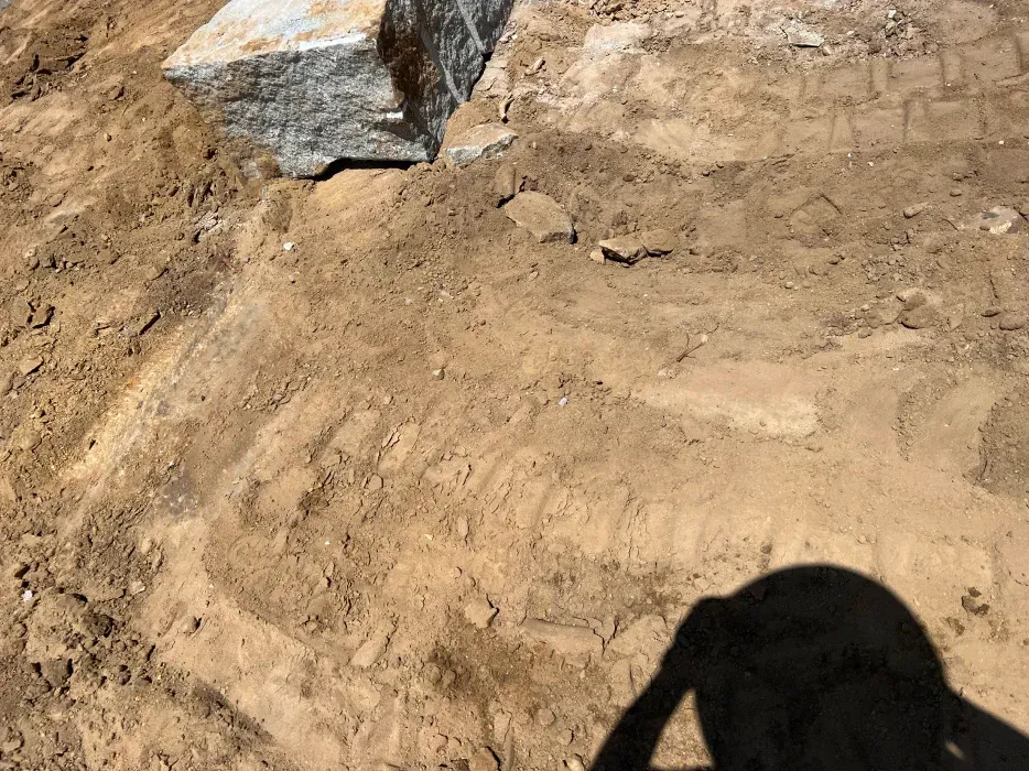 Brown dirt area with a large stone, possibly a construction site. A shadow of a person is visible.