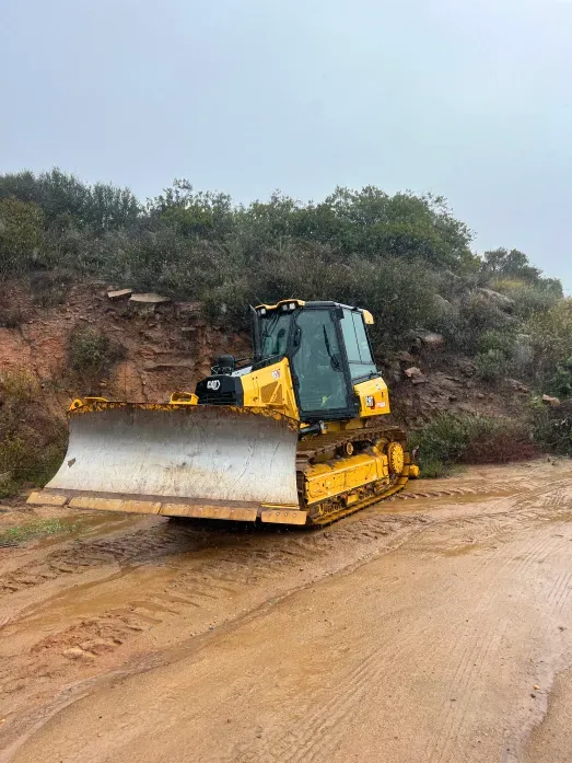 Yellow bulldozer on a muddy road near a hillside.