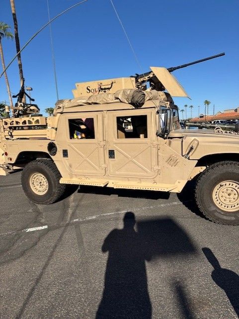 Tan military Humvee with machine gun mounted on top, parked outdoors on a sunny day.