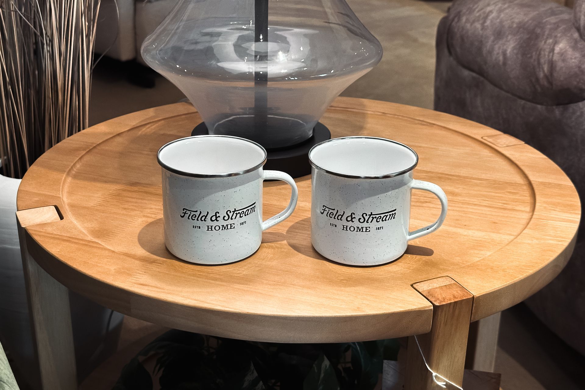 Two white mugs on a round wooden table in a cozy living room