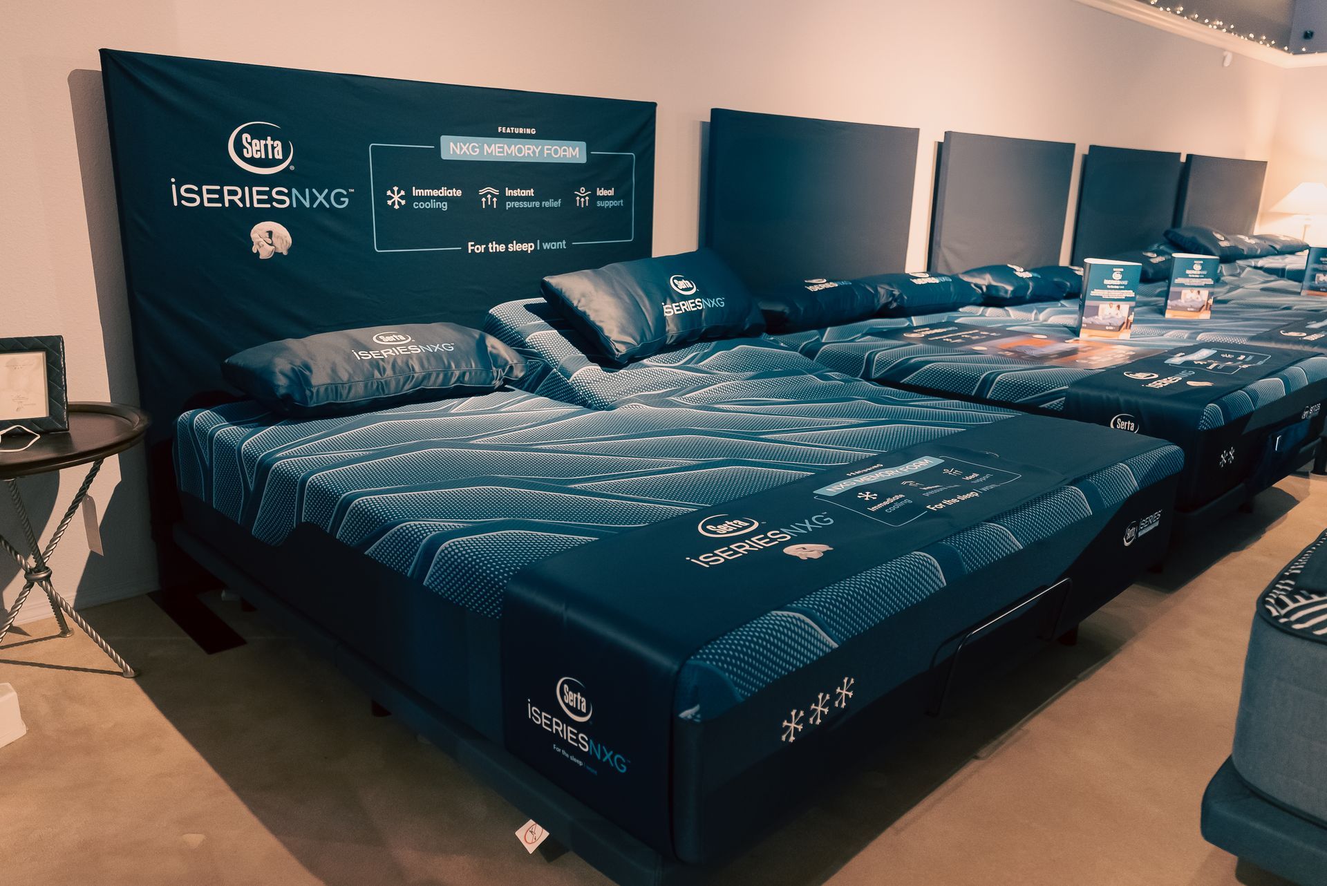 Mattresses and upholstered bed frames displayed in a showroom with dark blue bedding.