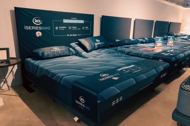 Rows of dark blue beds with white patterns in a showroom, displayed against a wall with matching headboards.