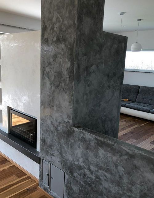 Modernes Wohnzimmer mit grauer, strukturierter Kaminwand und offenem Blick zum Ess- und Sofabereich