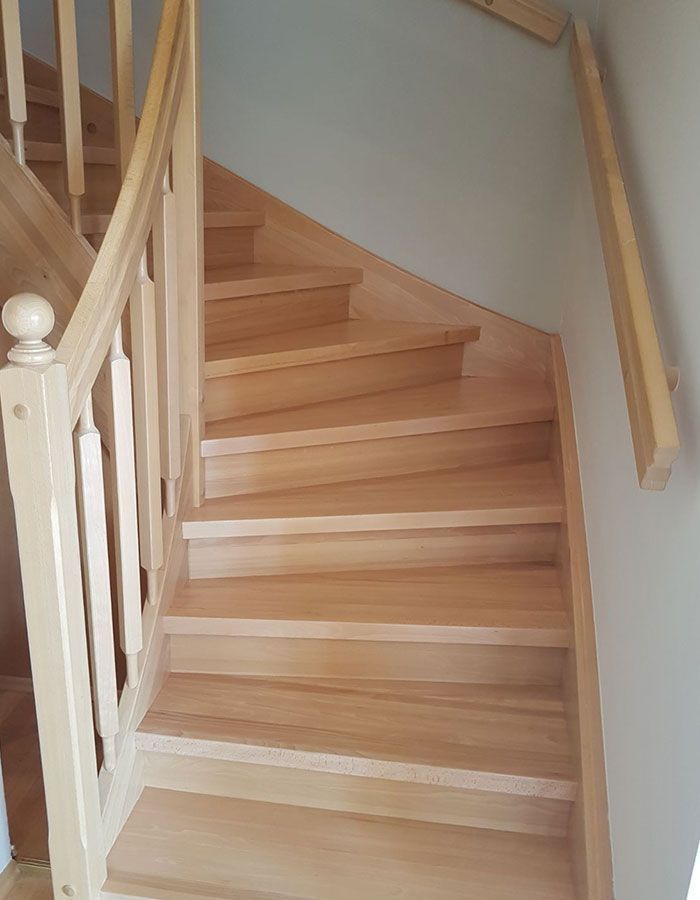 Holztreppe mit weißem Geländer und hellgrauer Wand im Wohnbereich.