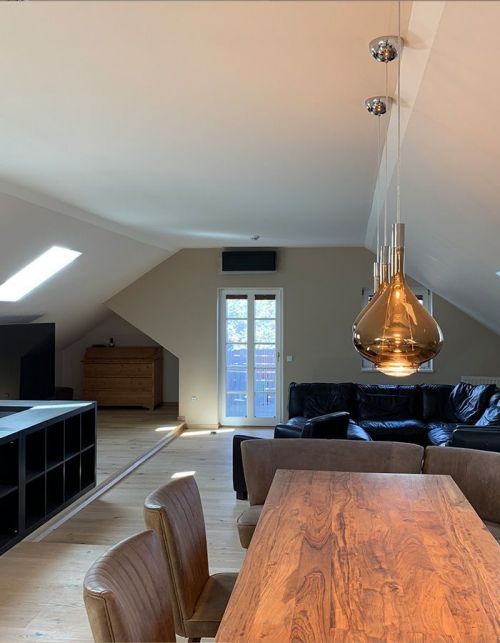 Modernes Loft-Wohn- und Esszimmer mit Dachschräge, schwarzem Sofa, Holztisch und Kupferpendelleuchte