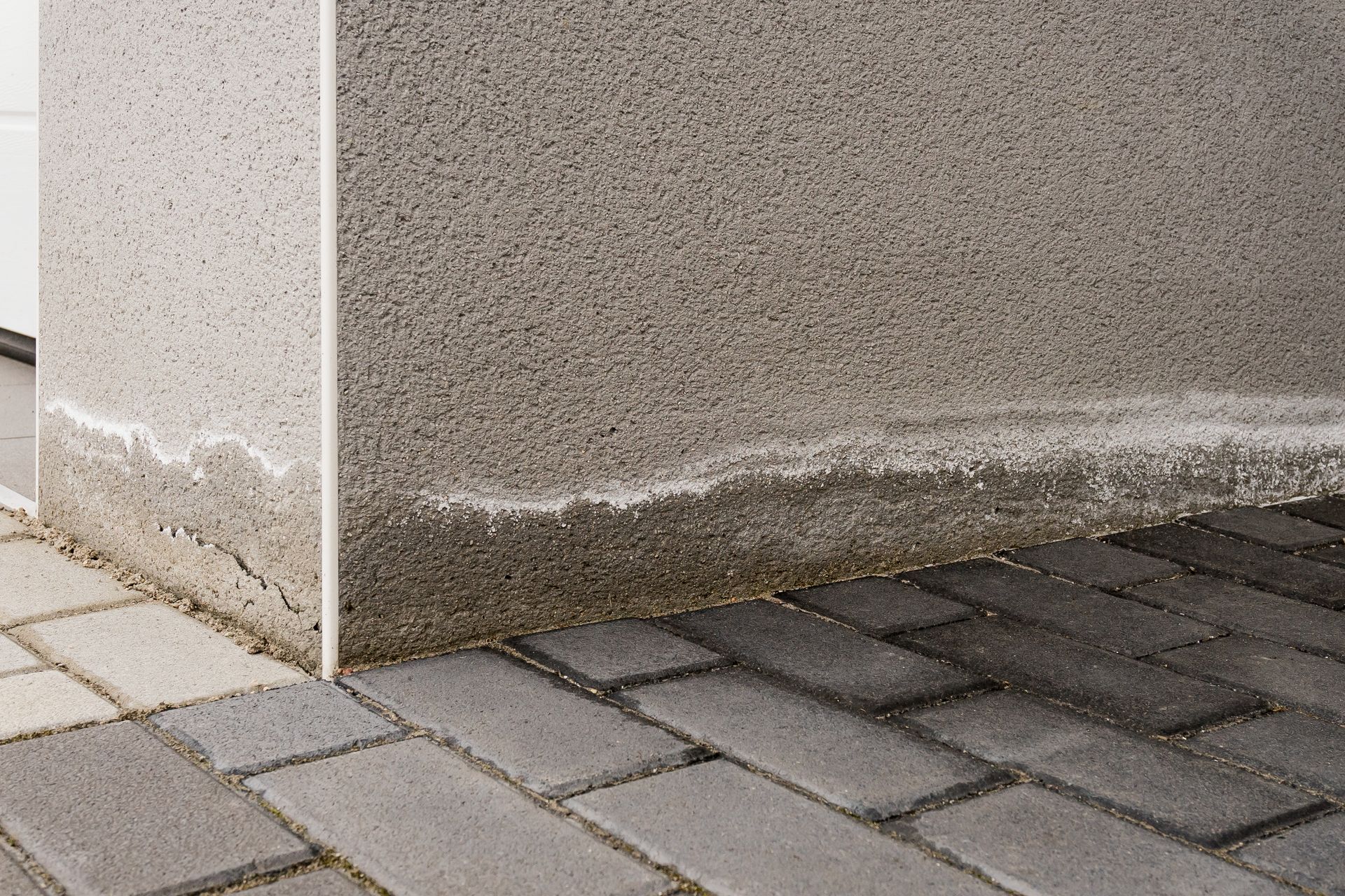 Untere Kante einer beigefarbenen Stuckwand mit weißen Feuchtigkeitsflecken neben grauen Pflastersteinen