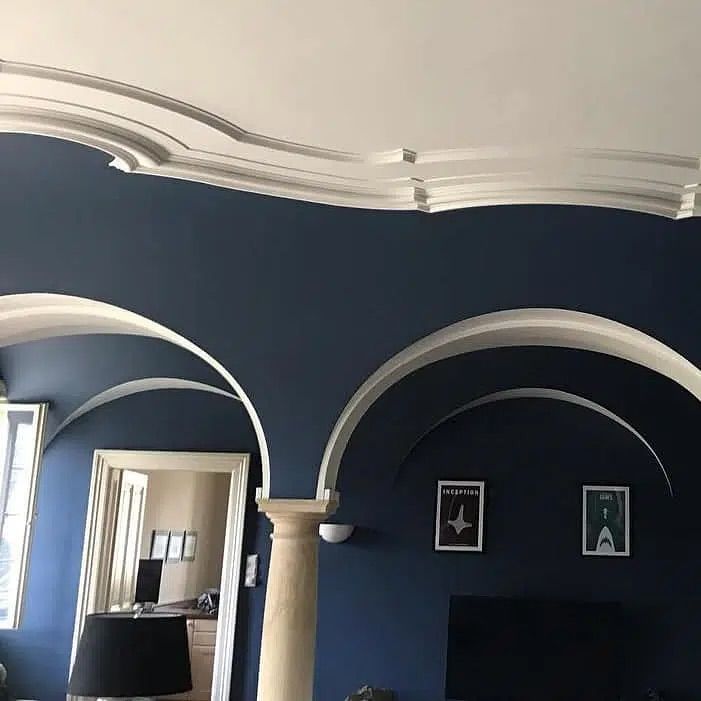 Blaues Wohnzimmer mit geschwungenen Wanddetails, weißer Deckenleiste und einem schwarzen Fernseher oder Kamin