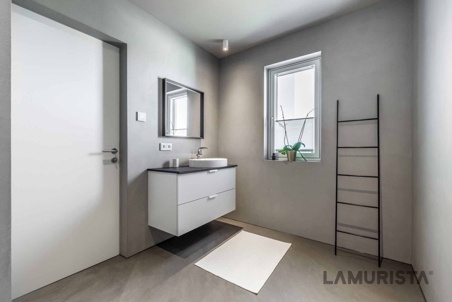 Minimalistisches, modernes Badezimmer mit weißem Waschtisch, Spiegel, Fenster und Handtuchhalter an grauen Wänden.