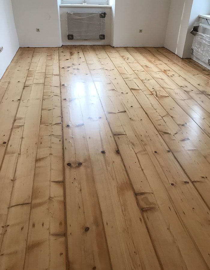 Ein leerer Raum mit hellen Holzdielen und einem kleinen weißen Heizkörper an der gegenüberliegenden Wand.