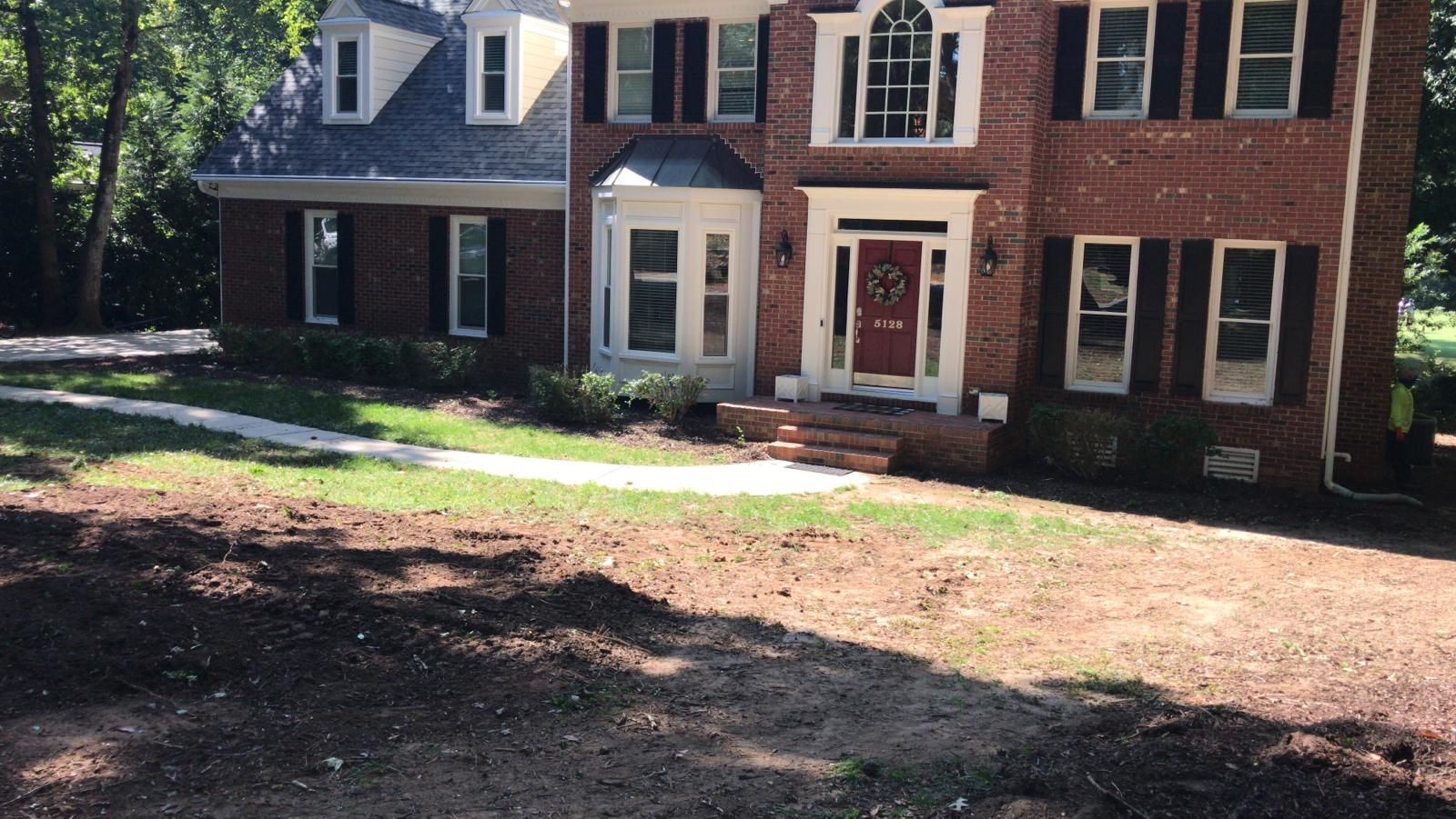 Large brick house with white trim and a front porch, seen from a dirt driveway in daylight