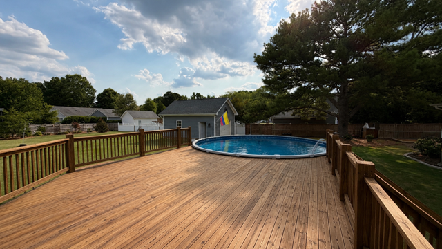 Backyard wooden deck beside an in-ground swimming pool under a partly cloudy sky