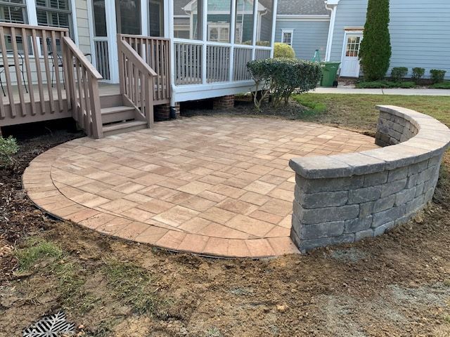 Curved brick patio with stone retaining wall beside a house deck and porch steps