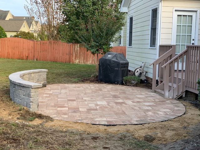 Backyard patio with curved stone bench and paved seating area beside a house