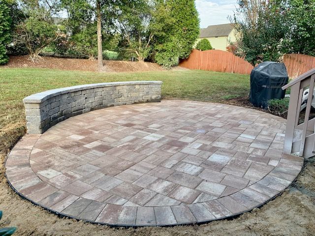 Circular stone paver patio with curved bench, set in a backyard with lawn and trees