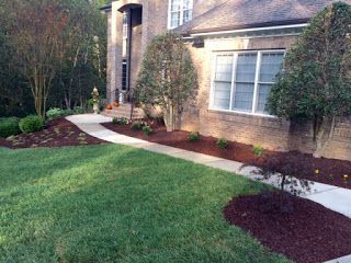 Front yard with green lawn, curved walkway, shrubs, and a brick house exterior with windows