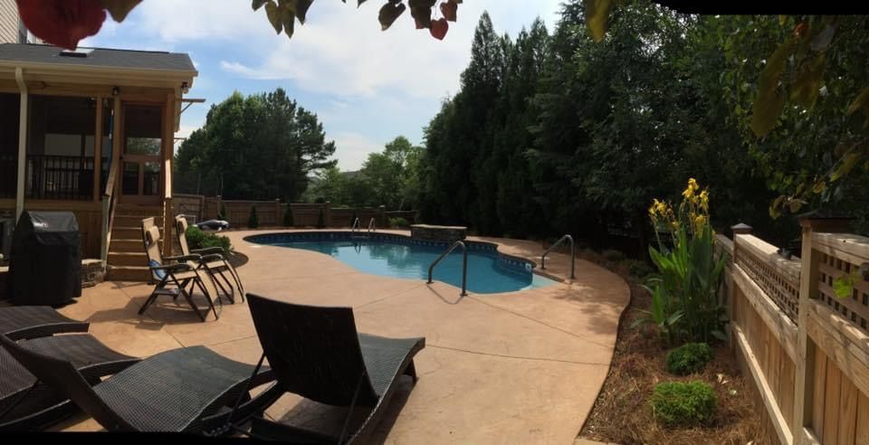 Backyard pool with lounge chairs, patio, and wooden fence on a sunny day