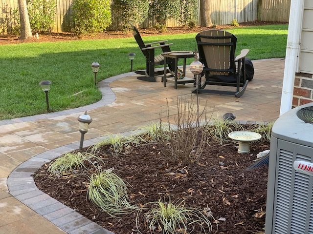 Curved stone patio path beside a mulched garden bed and outdoor seating in a backyard.