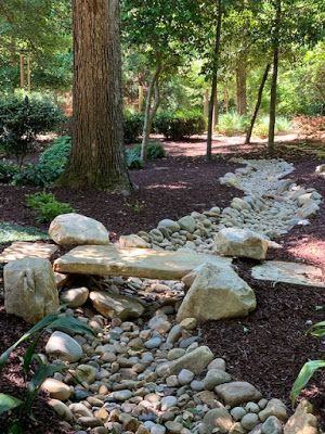 Rock-lined drainage ditch running through a leaf-covered wooded yard in winter.