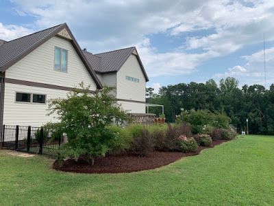 White house with gray roof and landscaped shrubs beside a wide green lawn under a cloudy sky
