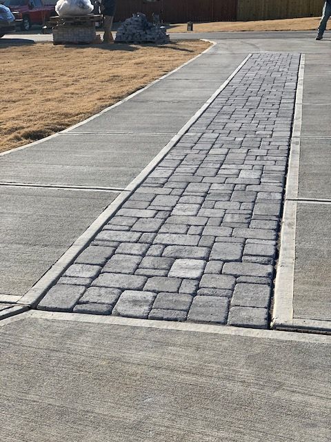 Curved concrete walkway with a central gray stone paver strip through a dry grassy park