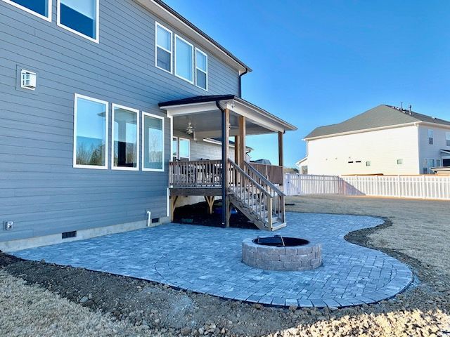 Backyard patio with blue pavers, fire pit, and wooden deck attached to a gray house