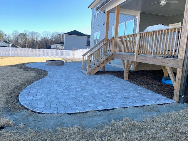 Curved stone patio beside a house deck and stairs in a snowy backyard