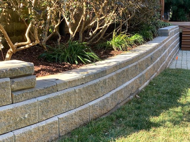 Curved stone retaining wall beside a landscaped garden with shrubs and grass