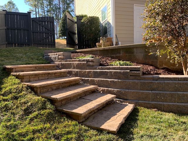 Wooden steps built into a grassy backyard slope leading to a raised patio beside a house