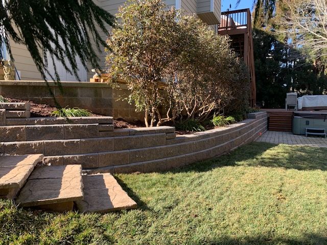 Backyard with stepped brick patio, shrub, and lawn beside a house