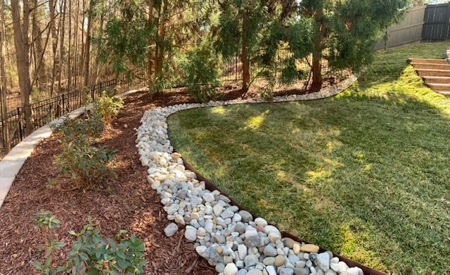 Curved rock border separating mulch and green lawn in a wooded backyard garden