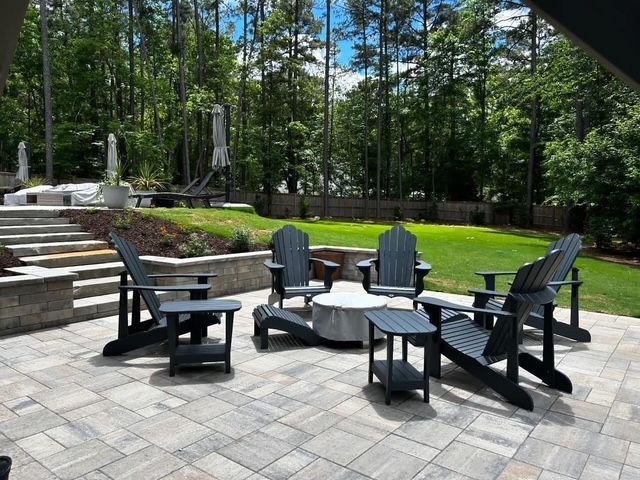 Patio seating with black Adirondack chairs around a fire pit in a sunny, wooded backyard