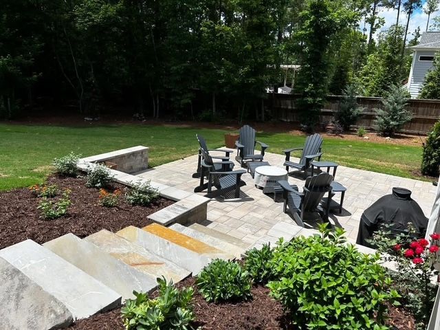 Backyard patio with steps, outdoor chairs, and a fire pit surrounded by trees and greenery