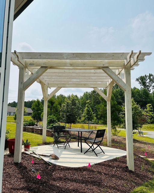 White wooden pergola shading a patio table and chairs on a landscaped garden walkway