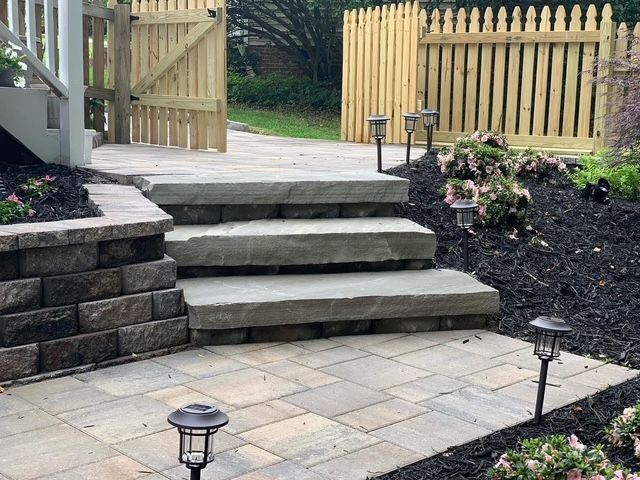 Stone patio steps leading to a wooden deck and gate, with landscaped garden lights and flower beds