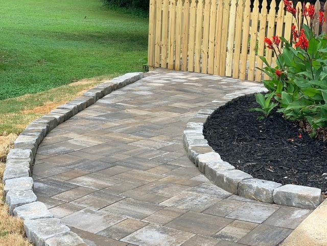 Curved stone paver walkway beside a wooden fence and flower bed in a landscaped yard