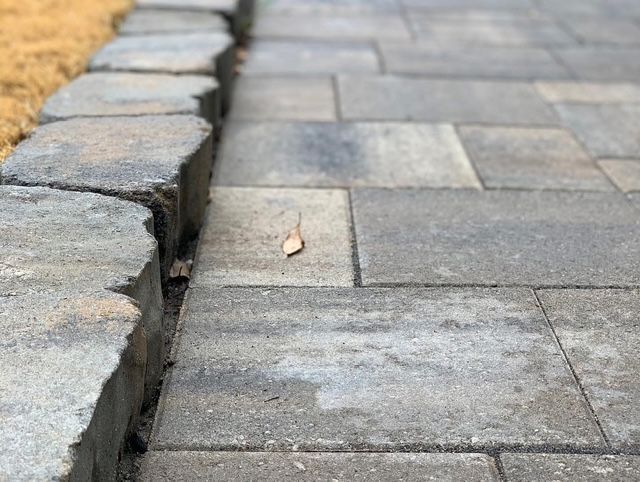 Stone curb beside gray paving stones with a small leaf on the walkway