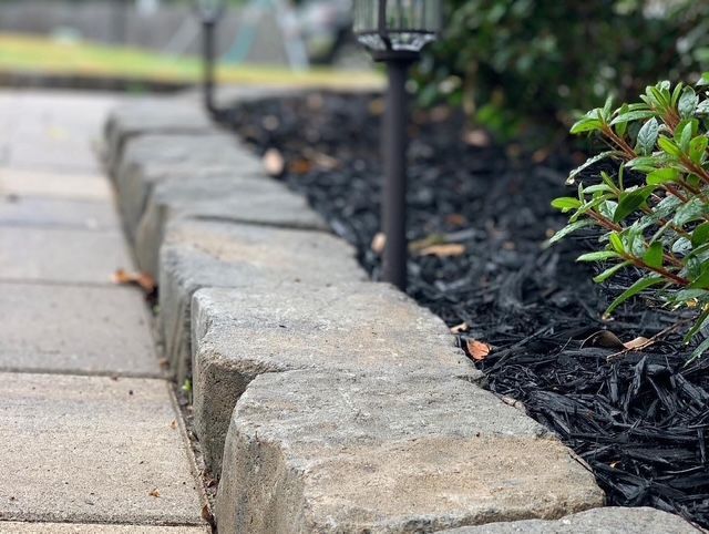 Stone garden border edging a sidewalk beside dark mulch and plants