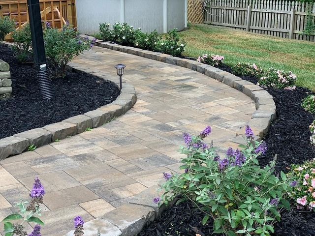 Curved stone garden path bordered by mulch and purple flowers beside a wooden fence.