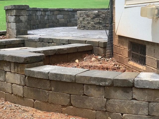 Stone steps and retaining walls beside a house, with a small planted area and green lawn.