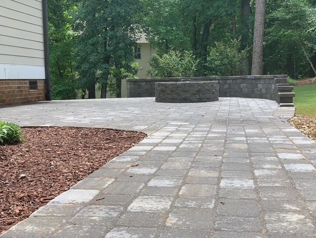 Stone patio path beside a house, with trees and a low stone wall in the background.