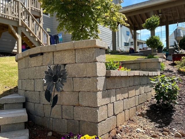Stone retaining wall with a black metal flower decoration beside a landscaped walkway and stairs